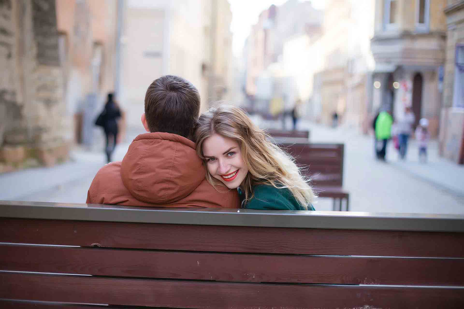 A Ukrainain woman leaning over a man’s shoulder while sitting at a bench.