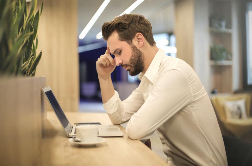 A photo of a man stressfully looking at his laptop