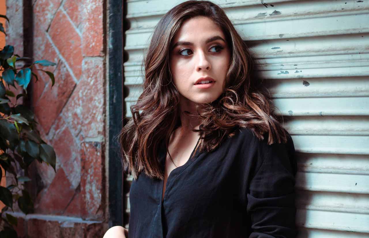 A photo of a woman in black dress standing in front of a roller shutter. 